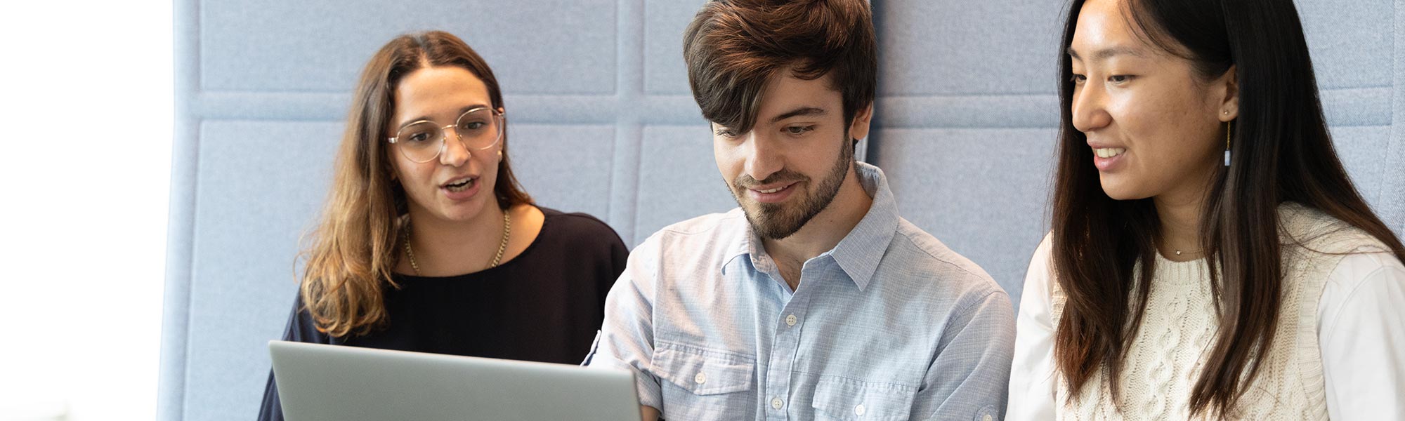 3 people interacting and smiling while working at a laptop.