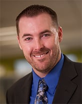 Man wearing a dark suit and tie in an office setting.