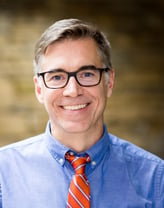 Brad Ketterling smiling in a blue shirt and orange tie.