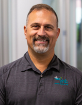 Bruce Marquis smiling in a VHB branded gray polo shirt.