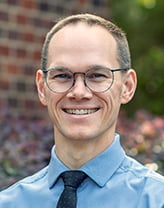 Bryce Corlett smiles outside wearing a blue shirt and tie 