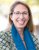 Headshot of Carol Lurie outside with her arms folded, wearing a blue scarf