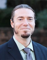 Man wearing a dark blue suit and tie in an outdoor setting