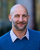 A man in a dark blue sweater over a light blue button up.