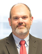 Kevin Fischer smiling in a brown jacket and pink tie.