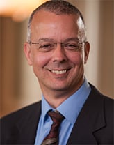 A smiling man wearing glasses and a suit