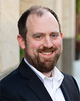 Mike in a shirt and jacket smiling in an outdoor setting