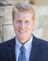 Mike Williard smiling in a blue suit.