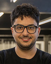 Nader in black shirt and glasses smiling in an office setting