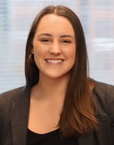 Paige Dickerhoof smiling in a brown blazer and black shirt.