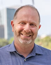 Man smiling at the camera in an outdoor setting.