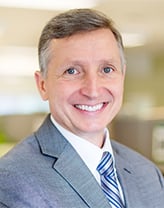 Tim wearing a gray suit and tie in an office setting.