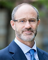 Tim wearing a dark blue suit and tie in an outdoor setting.