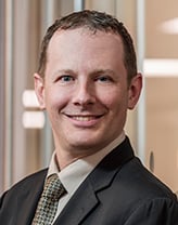 Tom Velleca in a dark brown suit and brown checkered tie