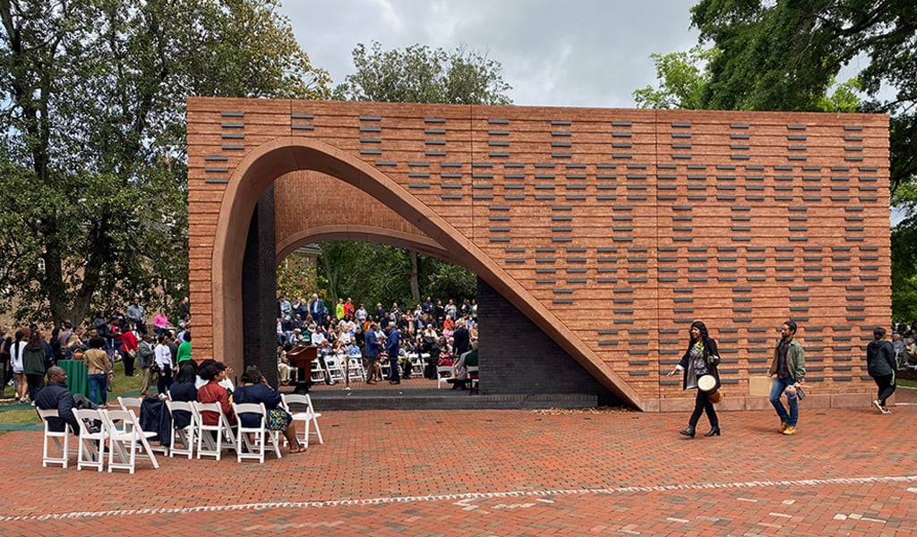 A view of the brick memorial during the memorial opening ceremony with people walking and sitting nearby.