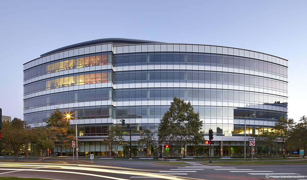 The curved glass wall office building at 300 Binney Street in Cambridge, Massachusetts is pictured at dusk.