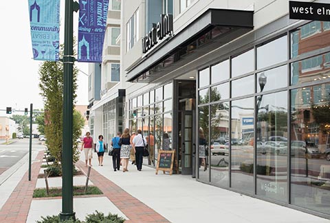 Pedestrians on the sidewalk stroll by retail establishments at Town Center of Virginia Beach.