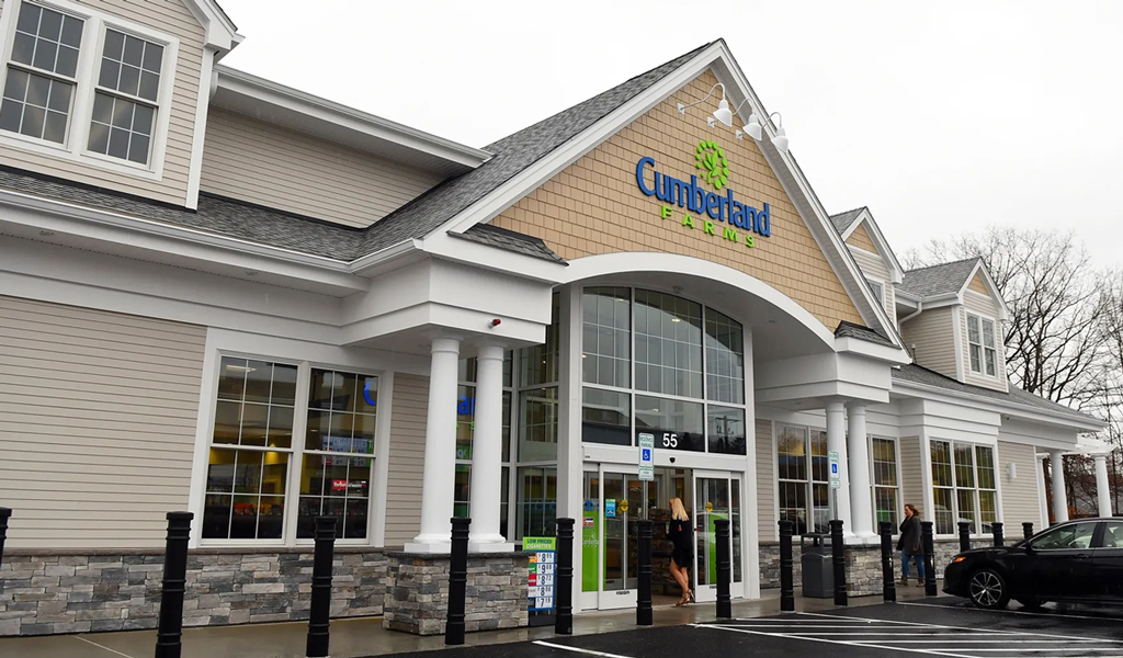 A modern Cumberland Farm store entrance with green and blue logo, stone façade, beige siding, and white pillars.