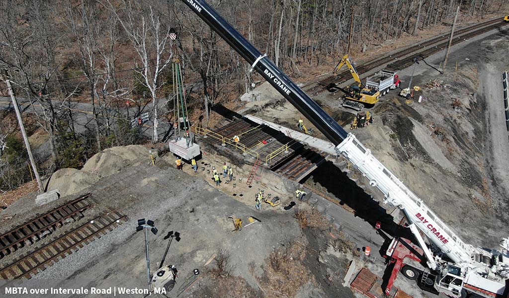 Workers use a crane and other heavy equipment to perform construction on an MBTA rail bridge over  Inervale Road in Weston, MA.