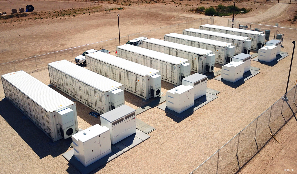 Battery Energy Storage System (BESS) arrayed in a gravel area enclosed with a tall chain link fence.