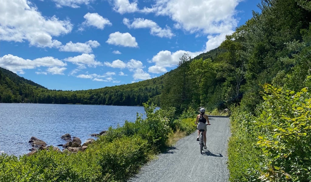 Woman riding her bike on the carriage roads adjacent to a pond. 