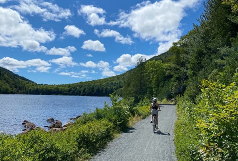 Woman riding her bike on the carriage roads adjacent to a pond. 