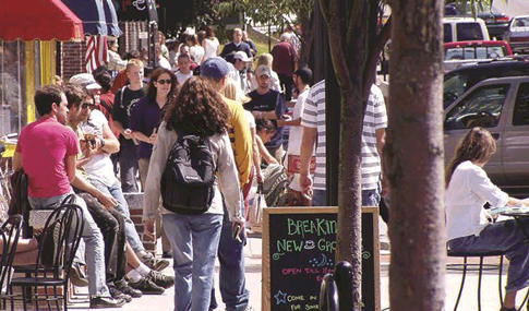 Pedestrians and bystanders share a crowded sidewalk.