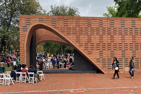 A view of the brick memorial during the memorial opening ceremony with people walking and sitting nearby.