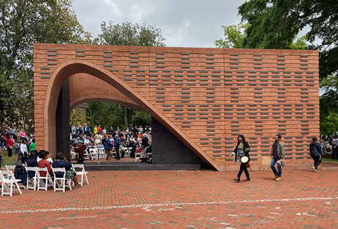 A view of the brick memorial during the memorial opening ceremony with people walking and sitting nearby.