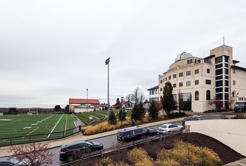 View of a sports field adjacent to a modern school building with a dome, under a cloudy sky  .