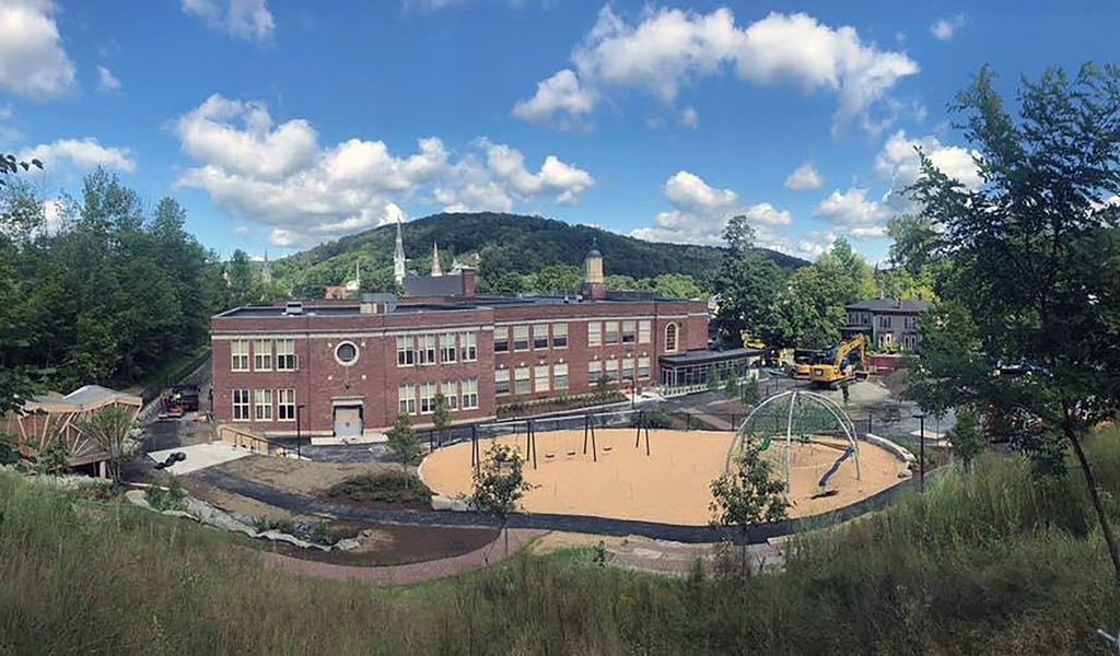 Soil and grass with construction equipment in front of a two-story brick elementary school