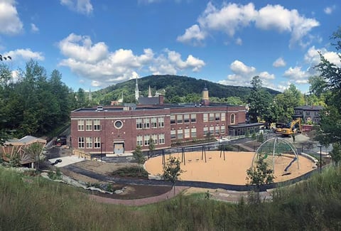 Soil and grass with construction equipment in front of a two-story brick elementary school