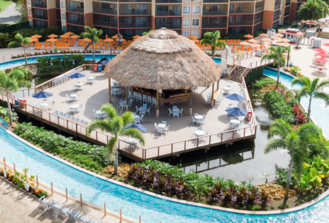 A cabana surrounded by lounging chairs, a lazy river, and greenery.