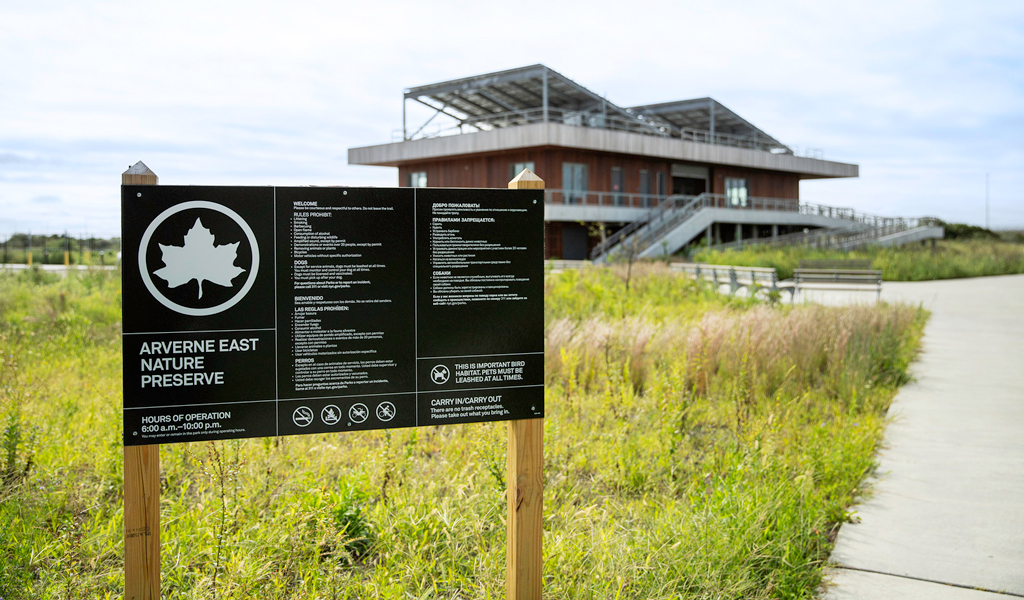 Sign for the Arverne East Nature Preserve in front of green grass and pathways.