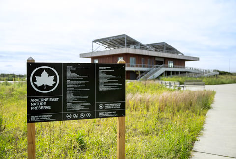 Sign for the Arverne East Nature Preserve in front of green grass and pathways.