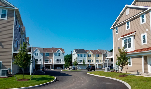 Road leading to light blue, yellow & tan multi-story residences at The Ridge at Talcott Mountain in Simsbury, Connecticut.