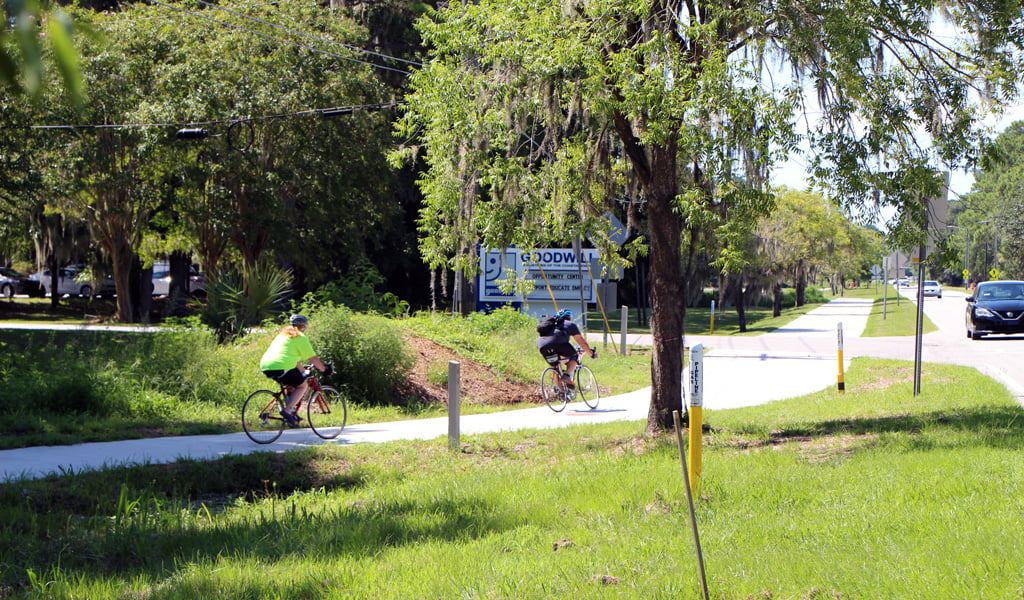 Two bicyclists wearing helmets ride on a suburban park trail.