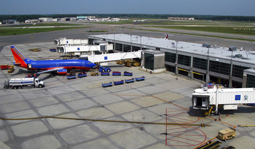 Exterior view of airport terminal, airplanes parked at gates, tarmac, and support vehicles.