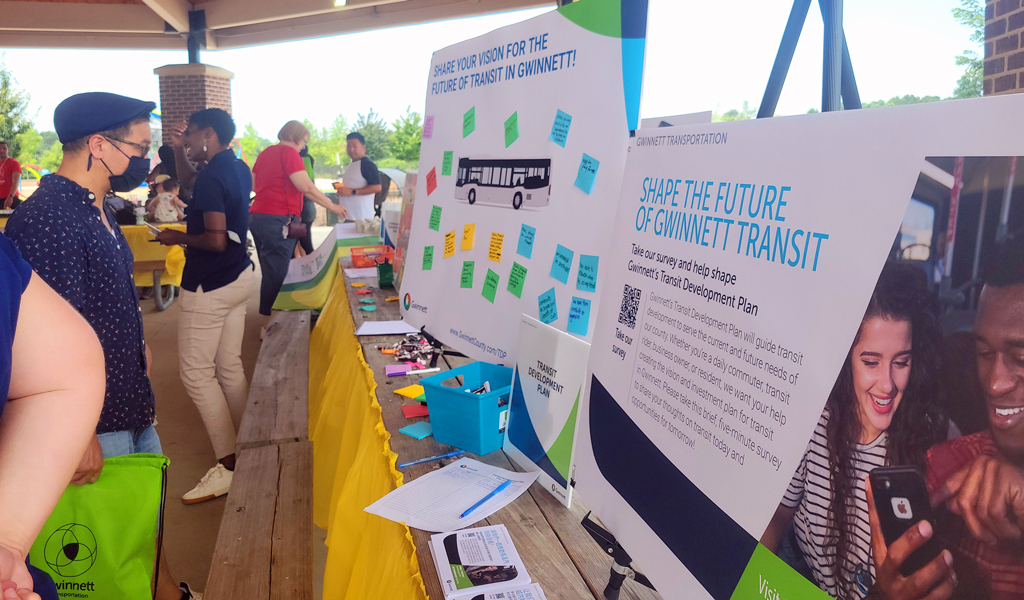 A man wearing a hat and face mask peruses presentation boards on a table.