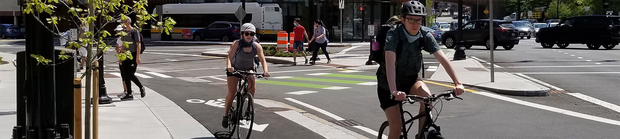 Two bicyclists ride in separated bicycle lane rounding an urban street and intersection.