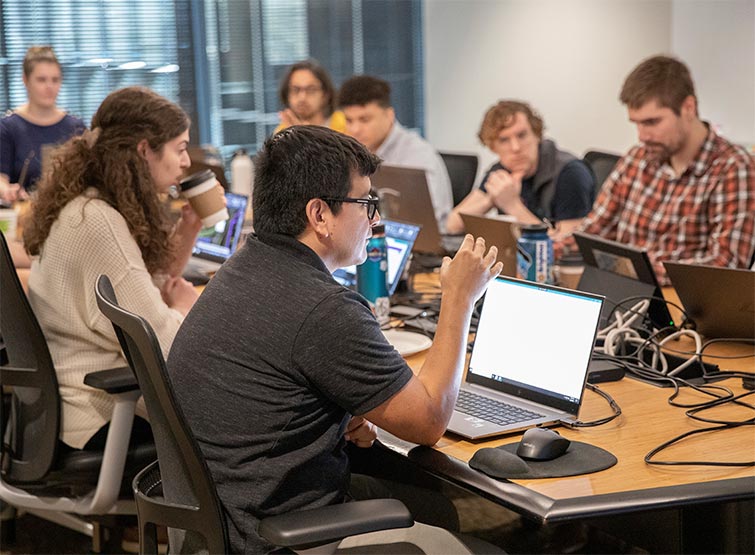 A group of people sitting at a table with laptops.