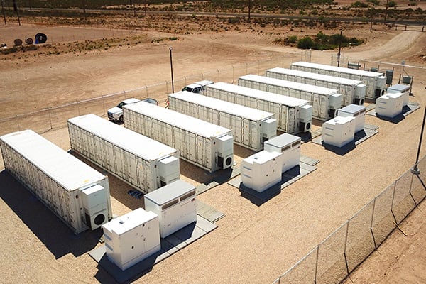 A row of eight (8) battery energy storage system units surrounded by a fence.