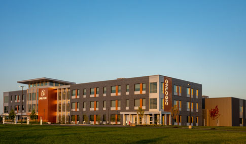 New commercial building at a distance with large lawn in foreground and blue sky.