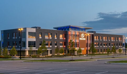 New commercial building at a distance with parking lot in foreground and cloudy skies.