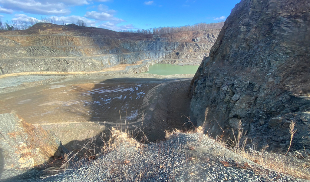 Landscape view down into the quarry with hills filled with gray gravel and a blue-green pond at the bottom. 