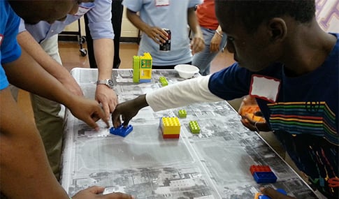 A child uses Lego blocks to add buildings to a map at a community forum.