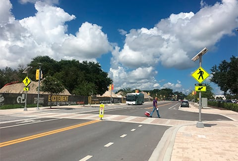 Man in a street crosswalk with yellow signs and an oncoming bus in the other lane. 