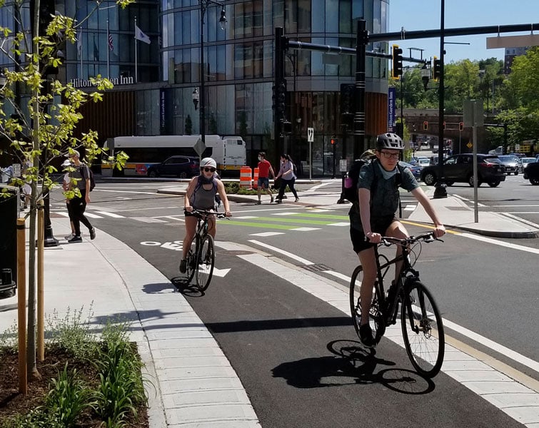 Bicyclists and pedestrians use designated lanes and crosswalks on a busy downtown street.