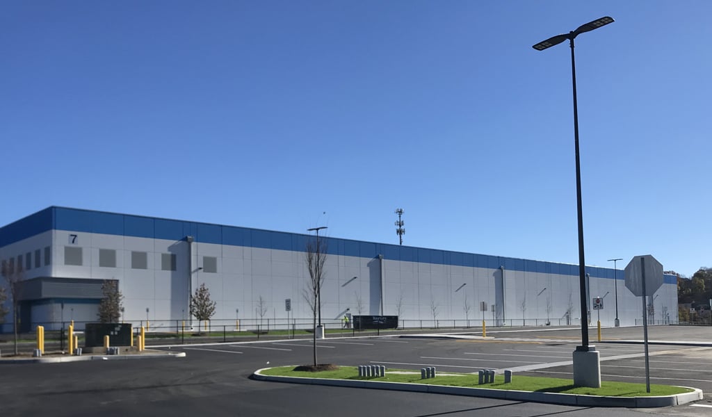 Exterior view of a large warehouse with a spacious parking lot under a clear blue sky.