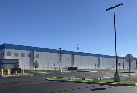 Exterior view of a large warehouse with a spacious parking lot under a clear blue sky.